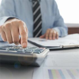 Man sitting at desk with reports, hand working a calculator, charts and stripped tie